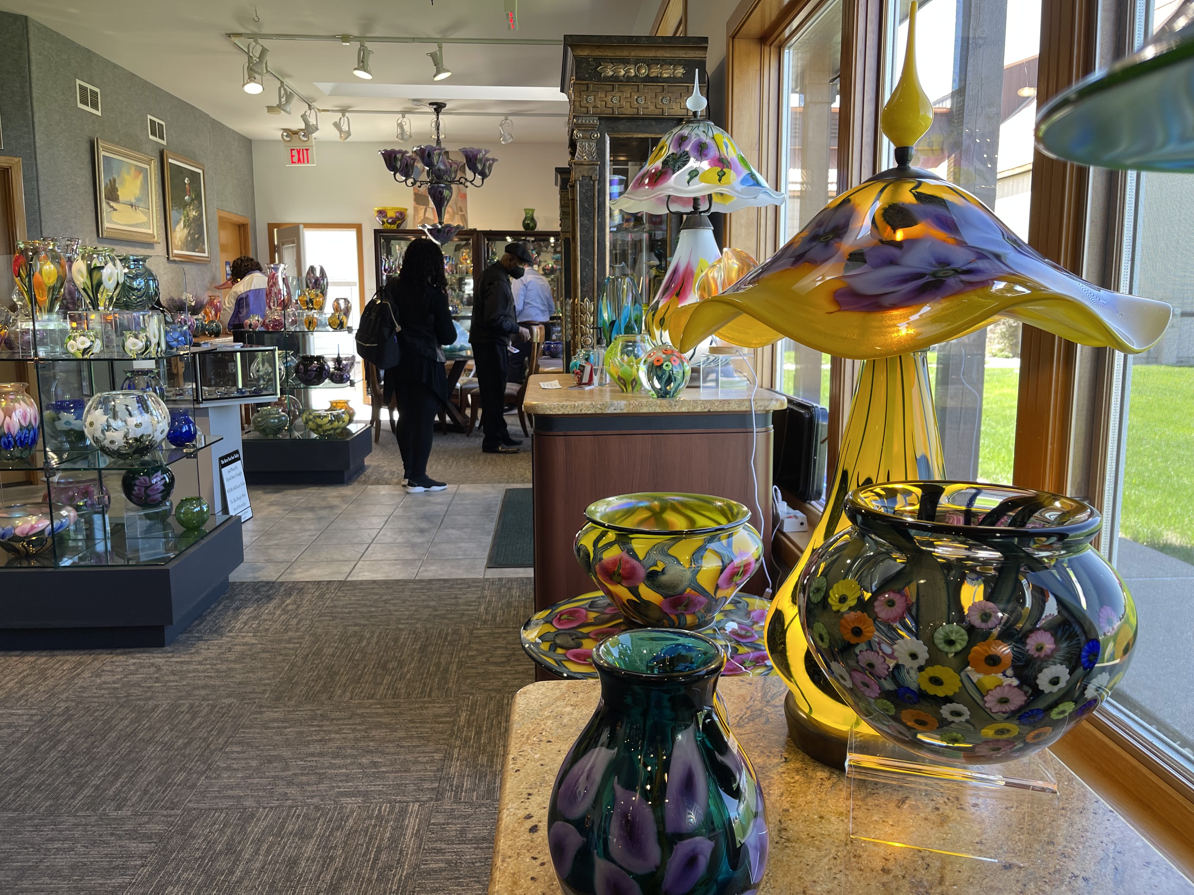 an art gallery with people in the baclkground and pieces of colorful aft including a lamp