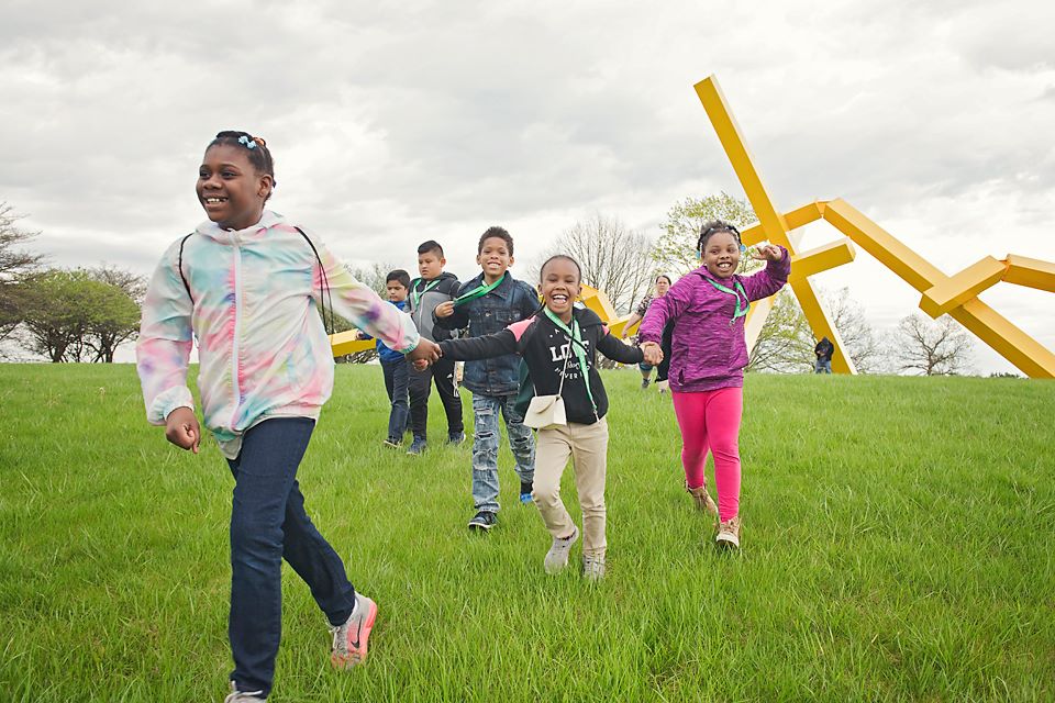 several kids with jackets on running by a sculpture