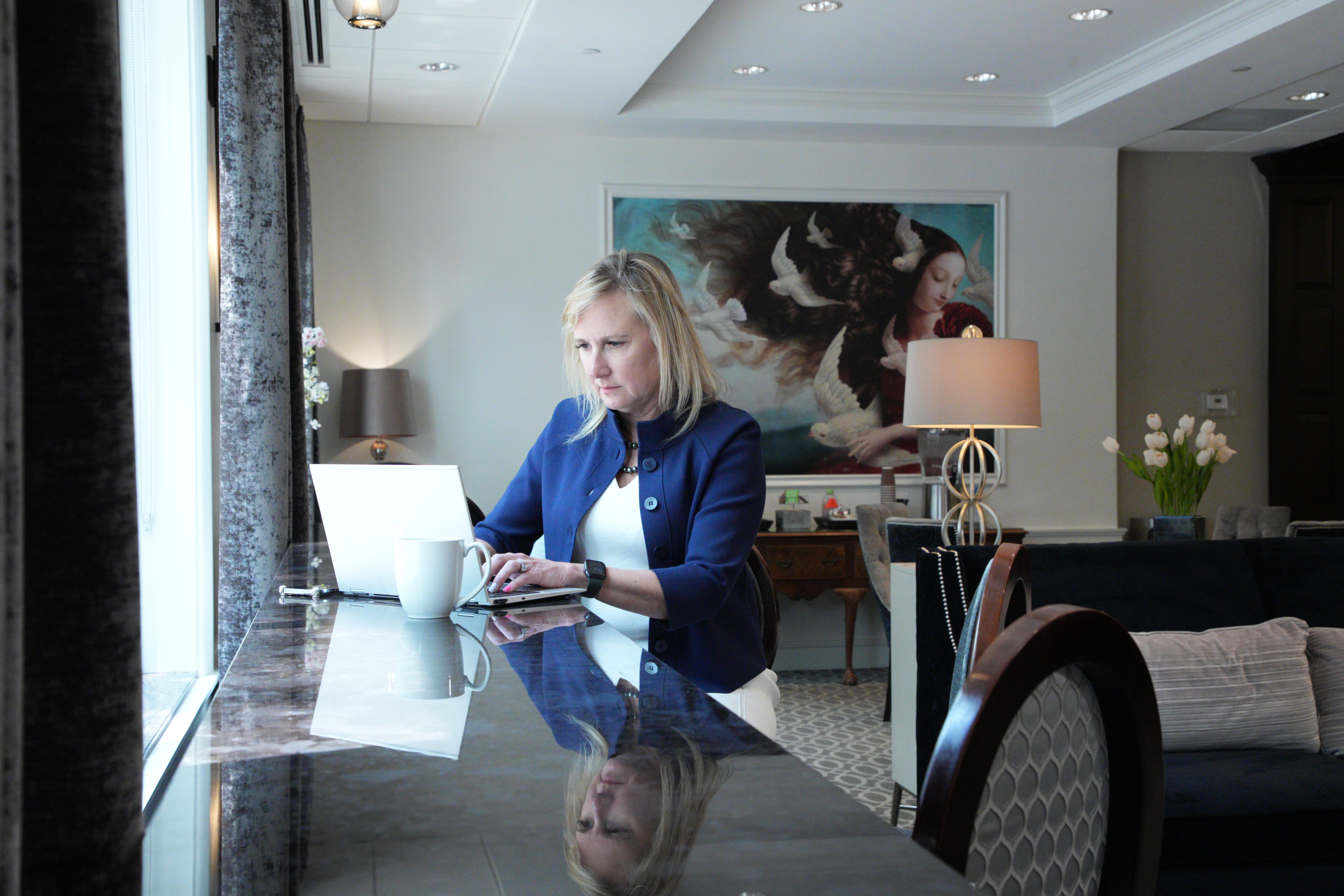 woman in a white dress and blue blazer sitting at a counter on her laptop