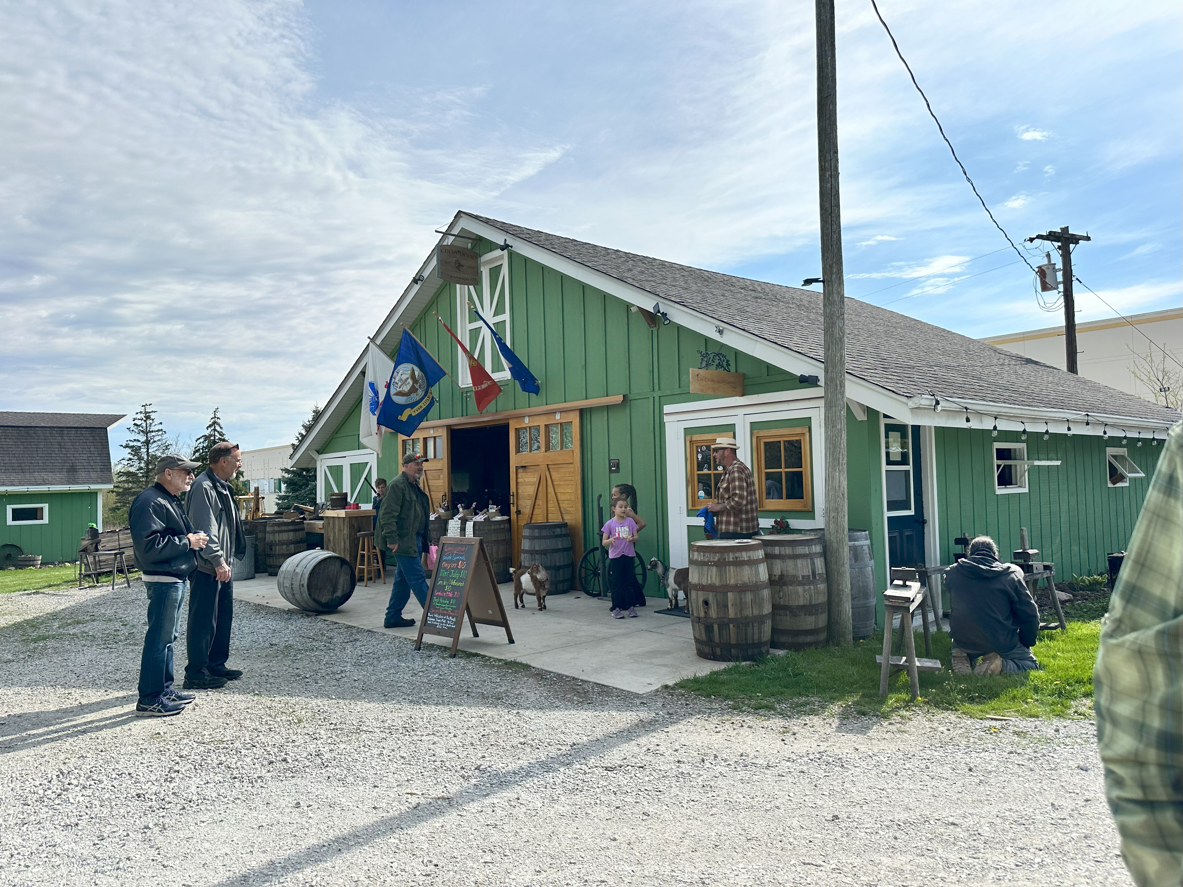 barn with people sitting outside drinking and socializing with goats in the background