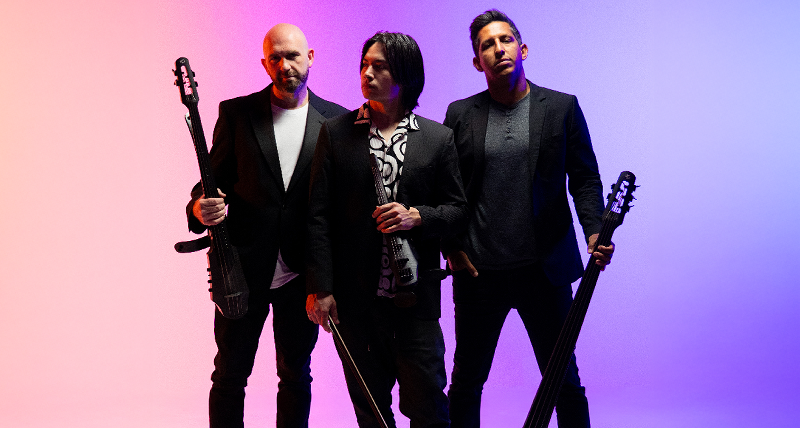 Three men holding instruments dressed in black jeans, boots and blazers