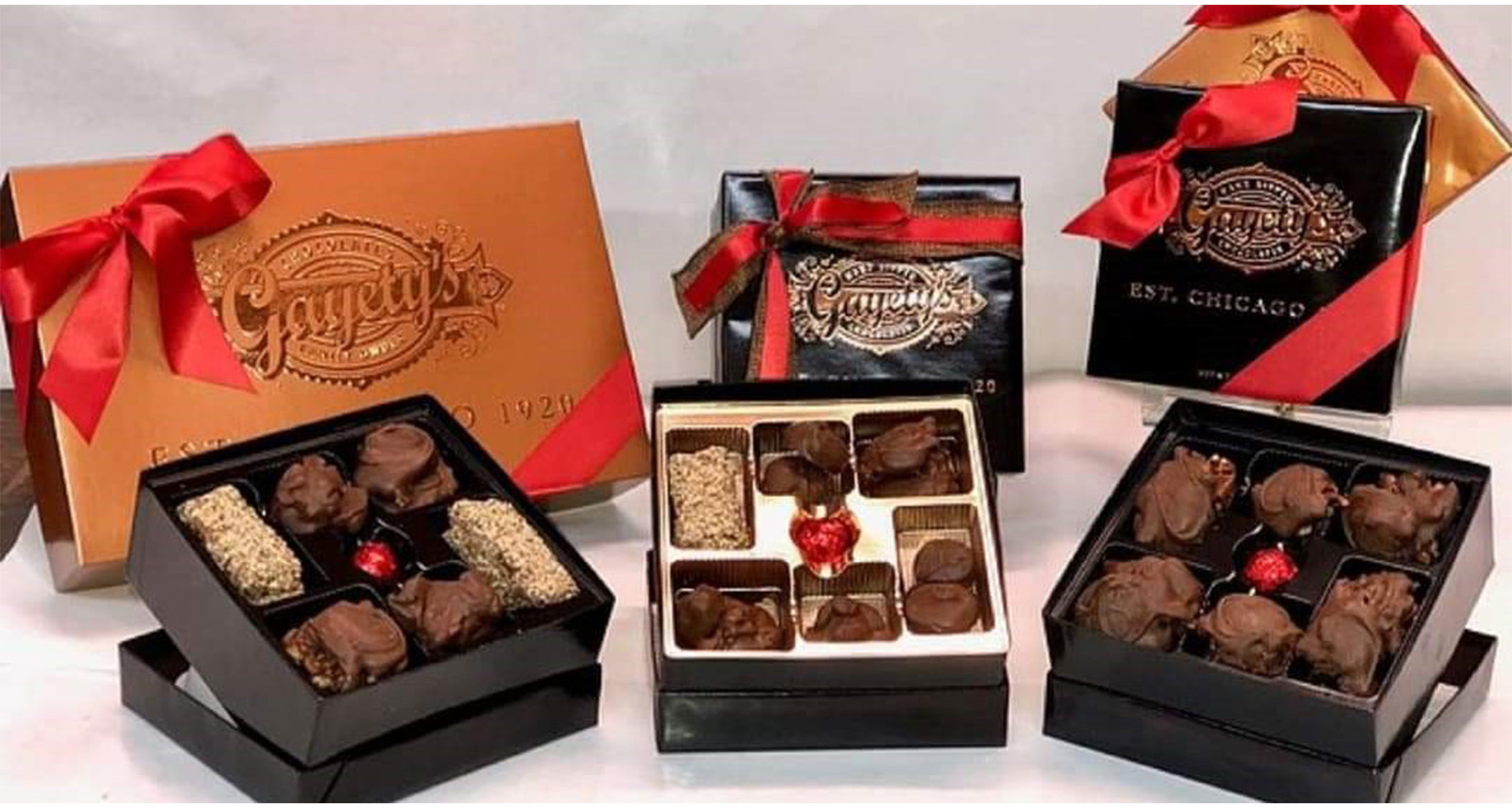 boxes of candy wrapped in a gold box with red ribbon and some boxes open with assorted chocolates - 